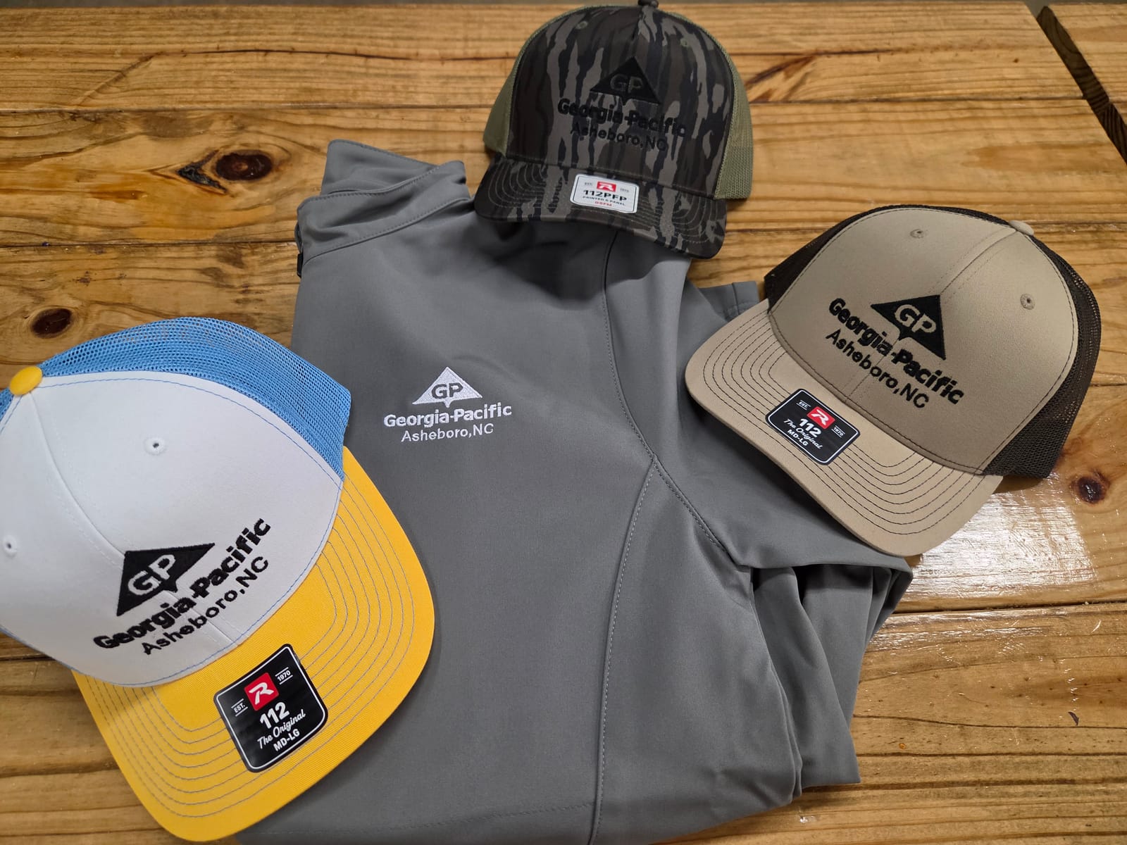 Embroidered Georgia-Pacific Asheboro logo on trucker hats and a soft-shell jacket